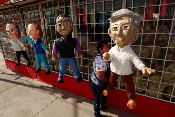 A woman hangs up pinatas for sale depicting Mexican presidential candidates Andr