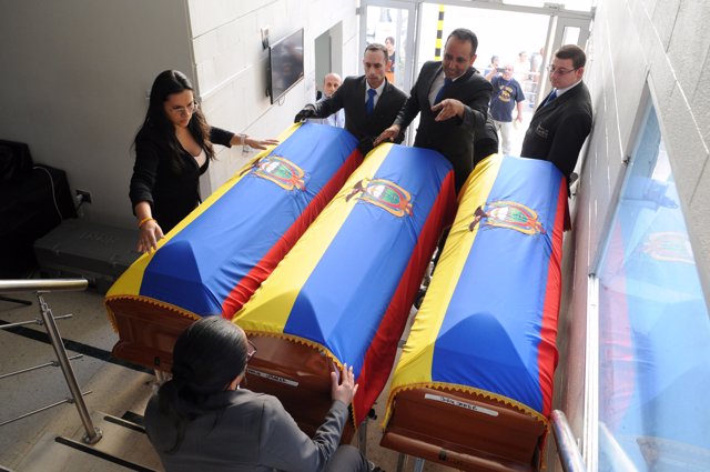 Funeral workers arrange Ecuadorean flags on top of coffins holding the dead bodi