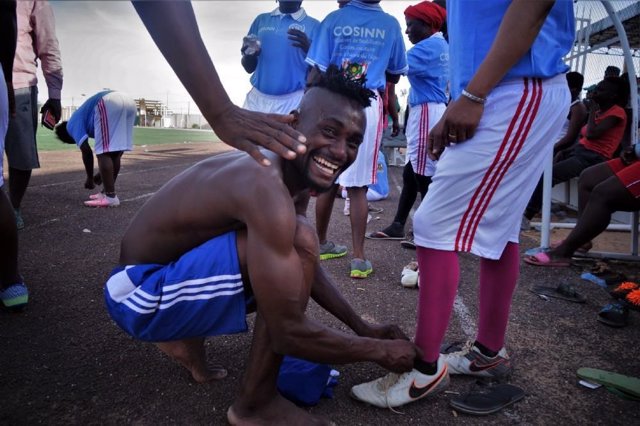 Un jugador del Nassara AC sonríe mientras ata las botas de su compañero 