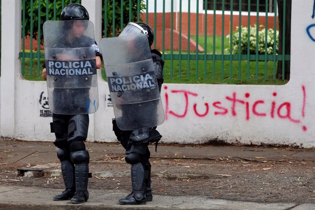 Riot police officers stand in front of a graffiti that reads "Justice" during a 