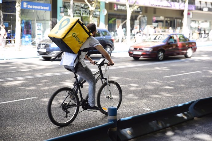 Treballador de l'empresa Glovo muntant amb bicicleta per Madrid 