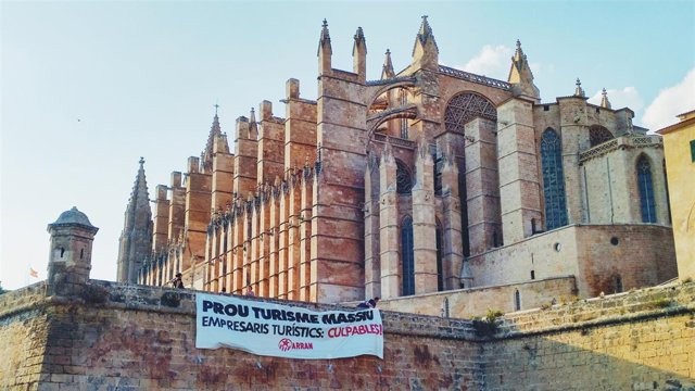 Arran cuelga un cartel contra el turismo de masas en la muralla frente a la Catedral