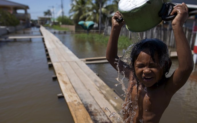 A boy pours water on himself as he stands on a makeshift walkway above a flooded