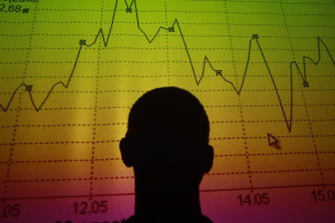 A man is silhouetted in an electronic board showing the FTSE MIB Index for the I