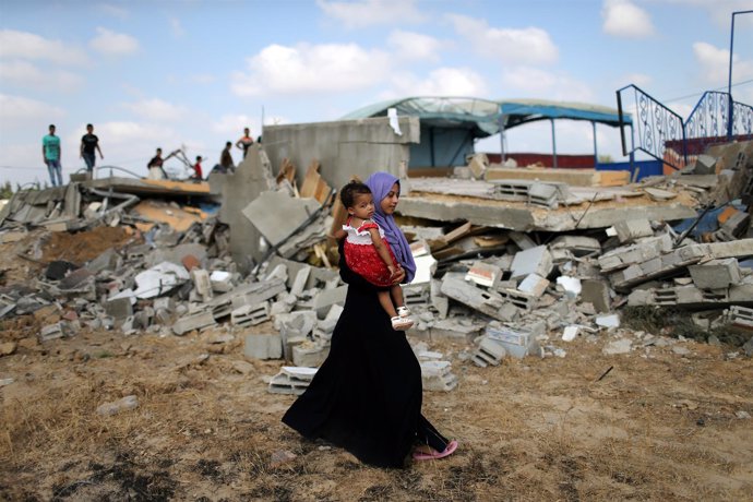 Una mujer pasea con su hijo por una zona bombardeada de Gaza