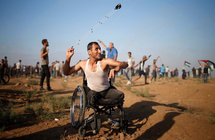 Un manifestante palestino en silla de ruedas lanza piedras hacia Israel