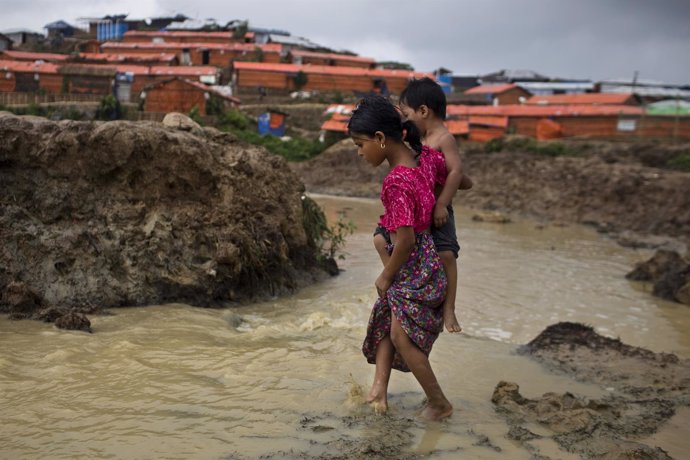 Una niña lleva a su hermano en un campo de refugiados rohingya en Bangladesh