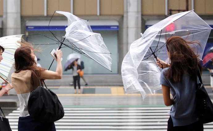 Unos peatones intentan controlar su paraguas ante el fuerte viento en Tokio