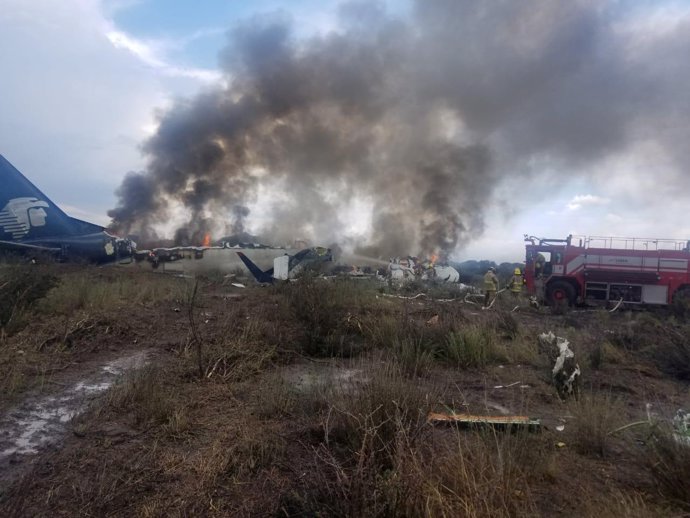 Firefighters douse a fire as smoke billows above the site where an Aeromexico-op