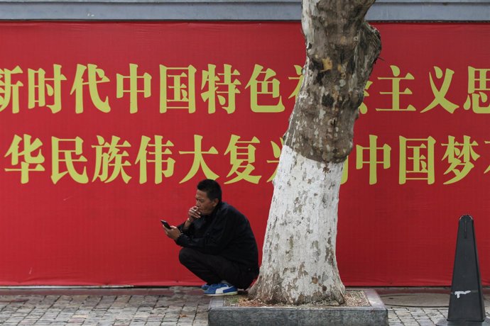 Un hombre mira su teléfono móvil frente a un cartel propagandístico