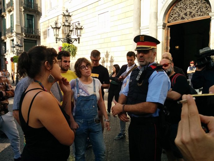 Membres de la CUP al costat d'un mosso en l'acampada de plaça de Sant Jaume