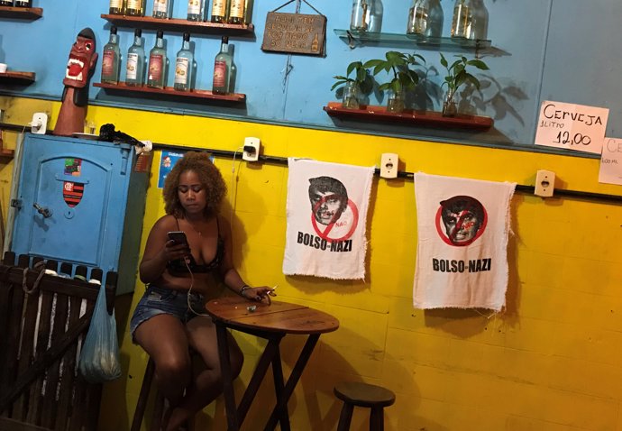 A woman sits next to signs with the image of Brazilian presidential candidate Ja