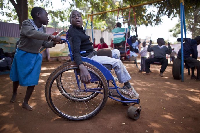 Una niña empuja a un niño con parálisis cerebral en silla de ruedas en Kenia