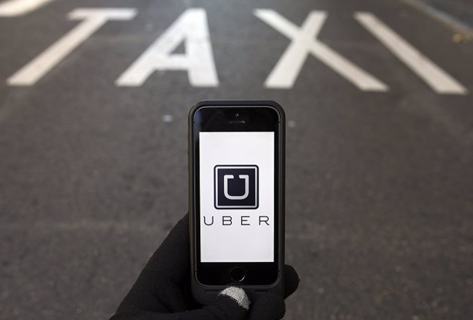 The logo of car-sharing service app Uber on a smartphone over a reserved lane fo