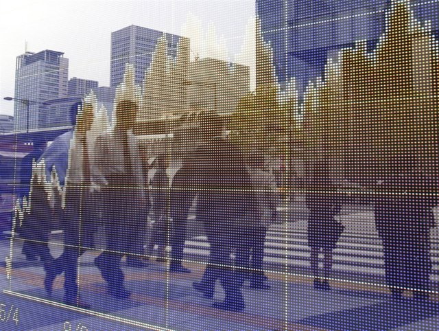 Pedestrians are reflected on an electronic board showing a graph of market data 
