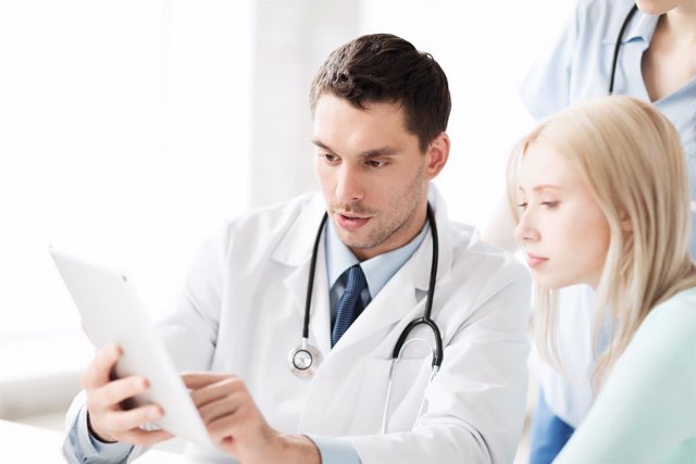 Consulta médico. Médico muestra una tablet a una paciente. Asistencia sanitaria.