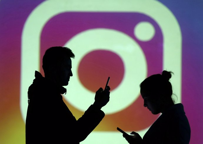 FILE PHOTO: Silhouettes of mobile users are seen next to a screen projection of