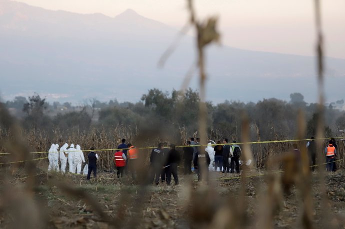 Forensic technicians and rescue personnel stand at the scene where the helicopte