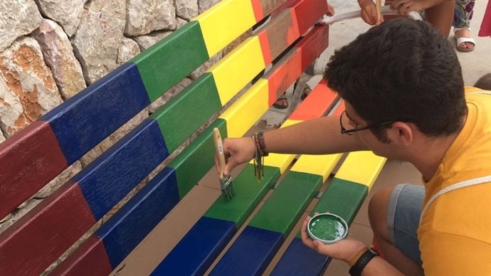 Un niño pintando un banco de los colores LGTBI