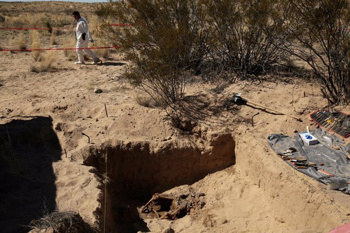 A forensic technician walks by a clandestine grave with skeleton remains at an a