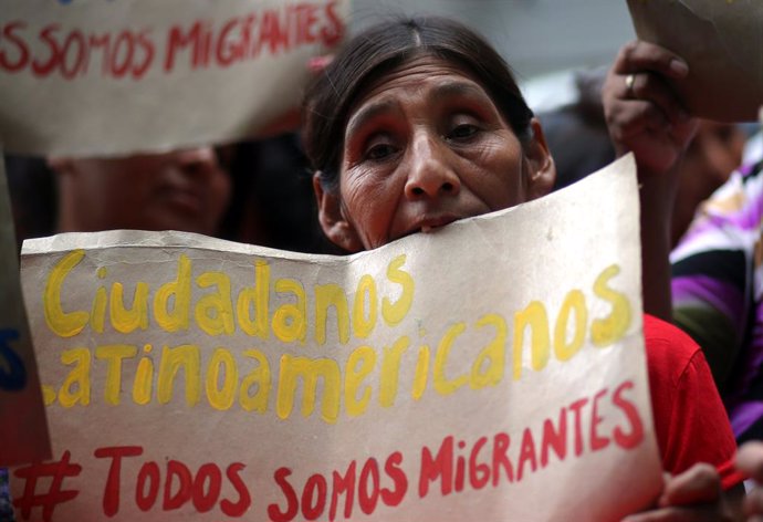 A demonstrator holds a sign that reads "Latin American citizens - We are all mig