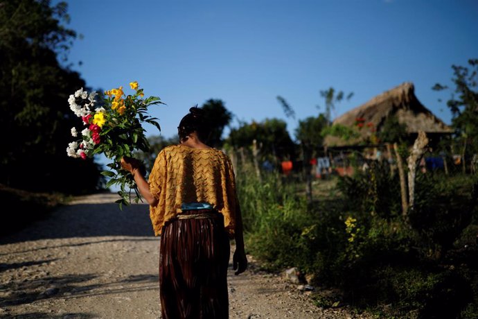 A woman walks with flowers near the home of Jakelin Caal, a 7-year-old girl who