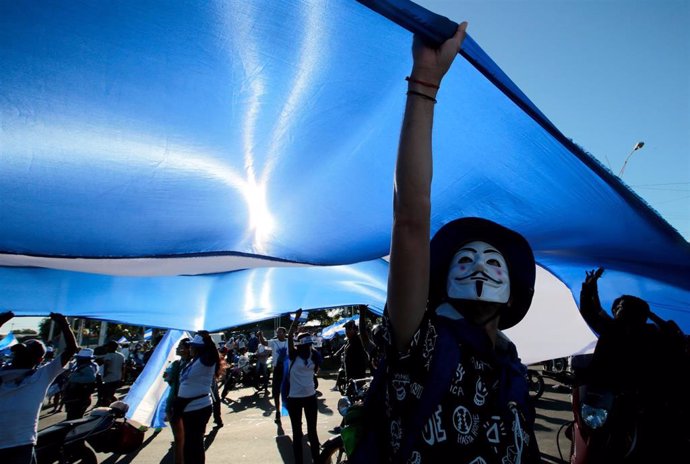 A masked demonstrator holds a big national flag during a protest against Nicarag