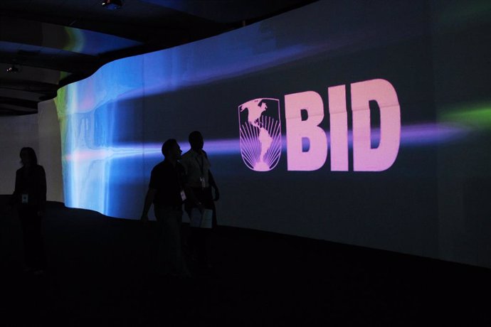 Visitors walk past a screen with the logo of Banco Interamericano de Desarrollo
