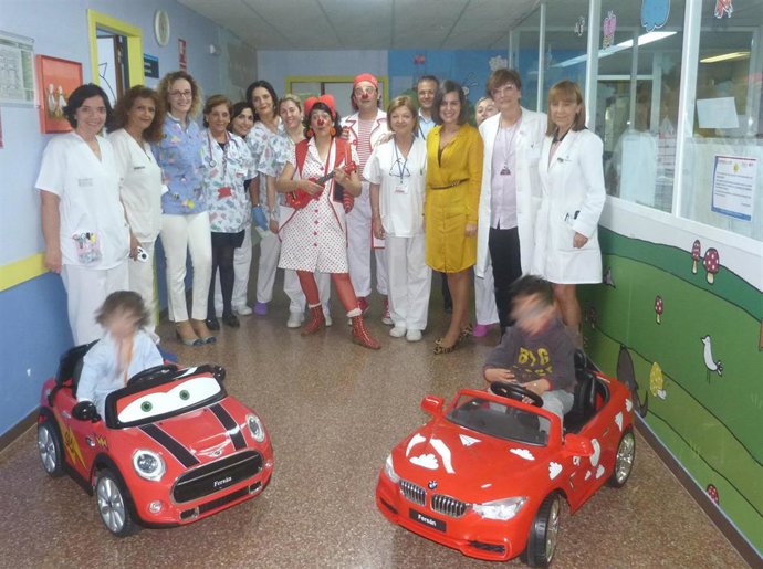 Los profesionales de pediatría junto a dos pacientes subidos a los coches.