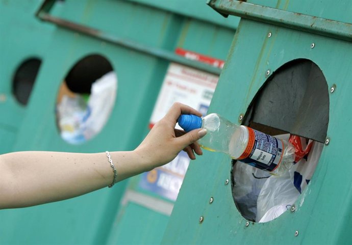 Una mujer tira al contenedor de plático una botella, reciclar, día del planeta