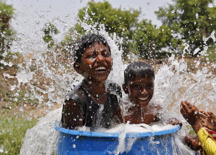 Dos niños alivian el calor en India bañándose en un contenedor.