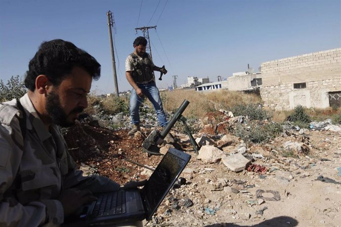 Un soldado del Ejército de Siria Libre usa un ordenador portátil mientras otro p
