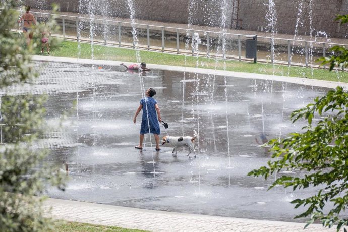 Una mujer se refresca con su perro en una fuente