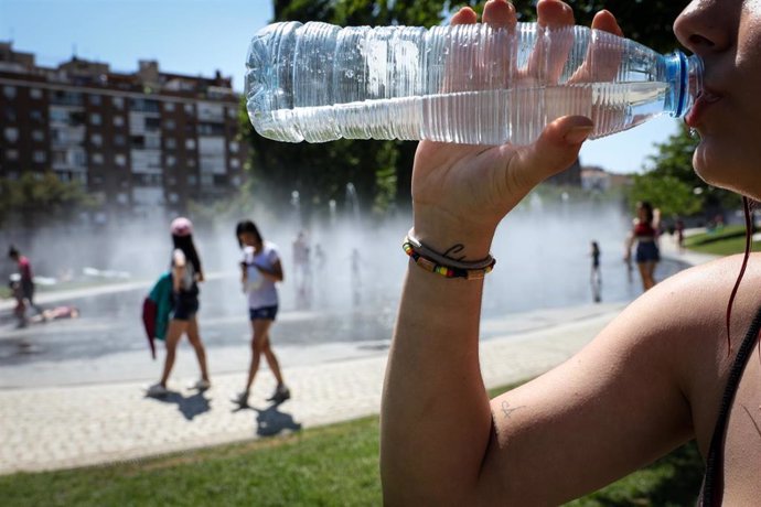 Una mujer bebe agua en una botella para refrescarse en las inmediaciones de los chorros de Madrid Río un día antes de que, según la Agencia Estatal de Meteorología (AEMET), llegue a la península Ibérica y a las Islas Baleares la primera ola de calor del