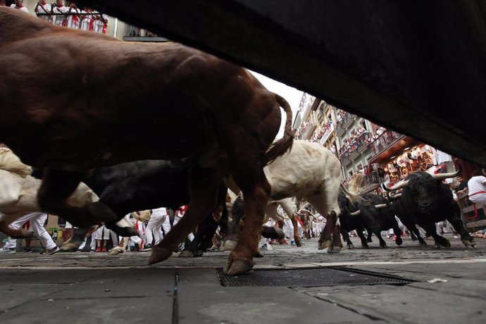 Decenas de personas corren delante de los toros en el primer encierro de las fiestas de San Fermín en Pamplona (Navarra).