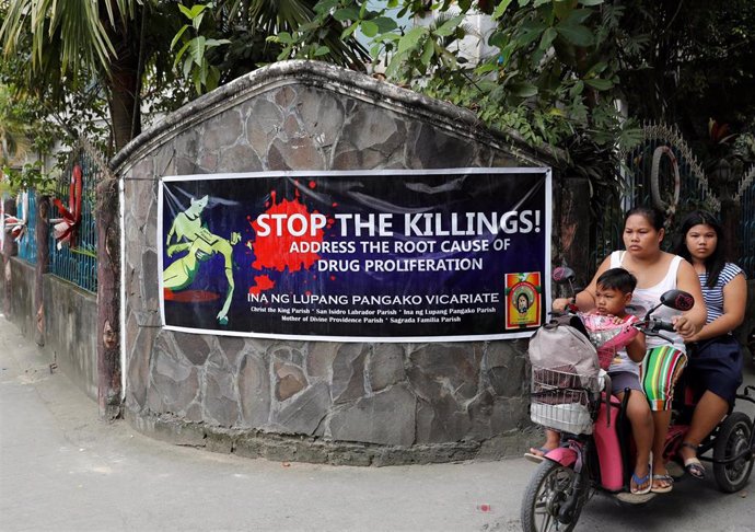 Una familia filipina pasa por delante de un cartel que reclama el cese de las muertes en la guerra contra las drogas