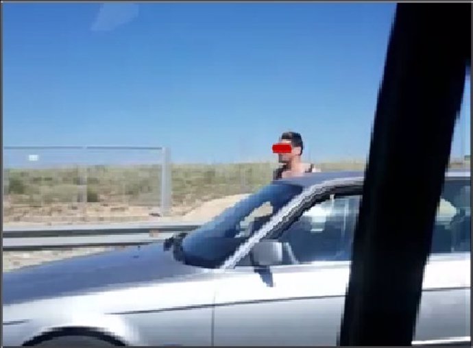 Imagen del vídeo grabado por una conductora en el que se aprecia al copiloto de un vehículo con medio cuerpo fuera.