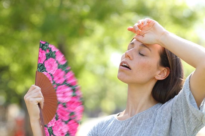 Mujer abanicándose en la calle con un abanico por las altas temperaturas y el calor de verano