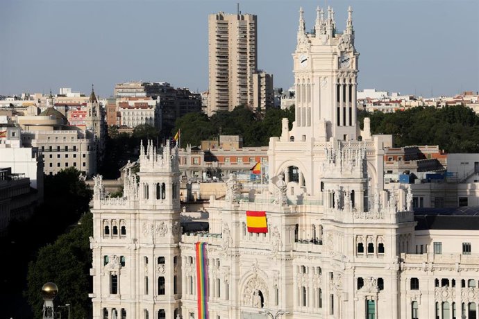 Fachada del Palacio de Cibeles de Madrid en la que se ha desplegado una segunda bandera de España y se ha colgado la bandera LGTBI en un lateral