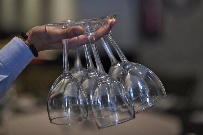 Un camarero sujeta copas de vino de cristal entre sus dedos. 