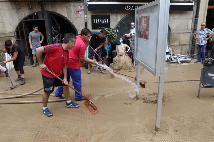 Varios vecinos limpian la calle tras las graves inundaciones en Tafalla.