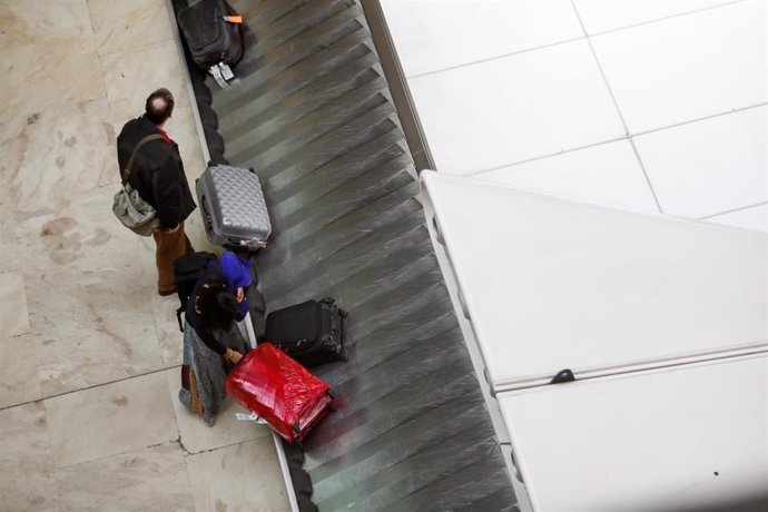 Un pasajero coge su maleta de la cinta transportadora,  junto a él, otro viajero espera a que llegue su maleta en el aeropuerto Adolfo Suárez Madrid-Barajas. 