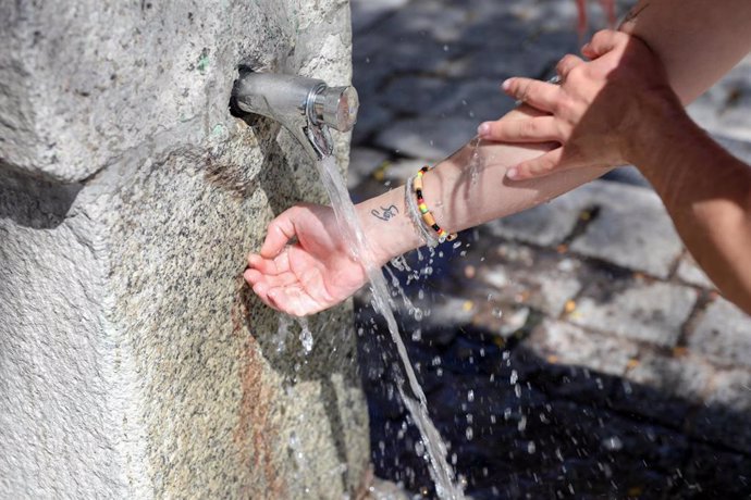 Un joven se moja las manos y brazos en una fuente para refrescarse de las altas temperaturas.