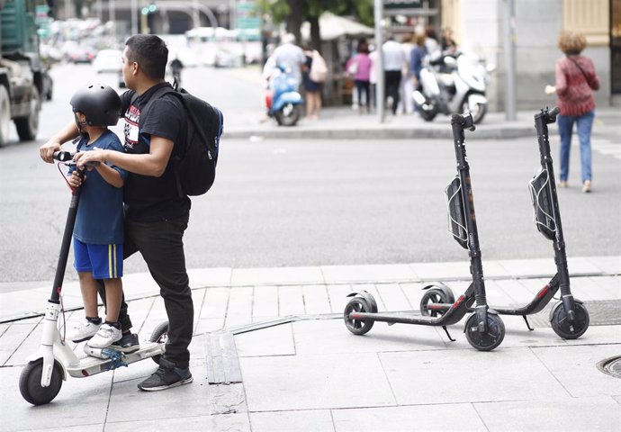 Un niño y un adulto montando en un patinete eléctrico en la calle Goya de Madrid.
