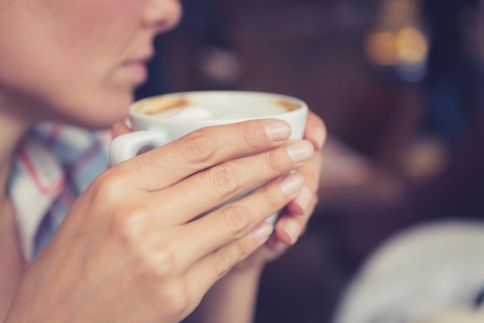 Single. Close up of woman hands holding a cup of coffee, sitting in cafe