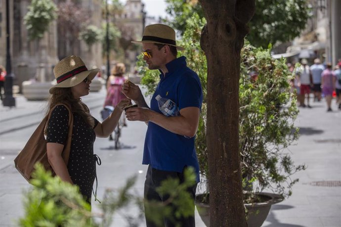 Pareja de turistas toman un helado bajo la sombra de un árbol en la Avendia de la Constitución de Sevilla