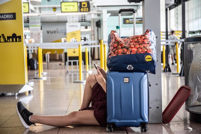 Un joven mira su movil sentado junto a su maleta, junto al puesto de la compañía, Vueling en el Aeropuerto 'Josep Tarradellas Barcelona-El Prat', durante la Huelga del personal de tierra de Iberia en Barcelona.
