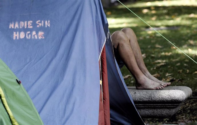 Uno de las casi  80 acampados sin techo de Madrid que llevan pernoctando desde hace tres meses en el Paseo del Prado está tumbado en un banco al lado de una tienda de campaña con la frase impresa 'nadie sin hogar'. La acampada reclama al Ayuntamiento de
