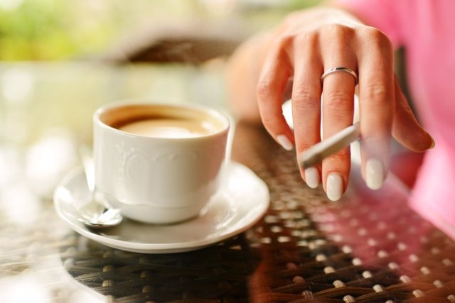 Mujer tomando café y fumando en la cafetería al aire libre.