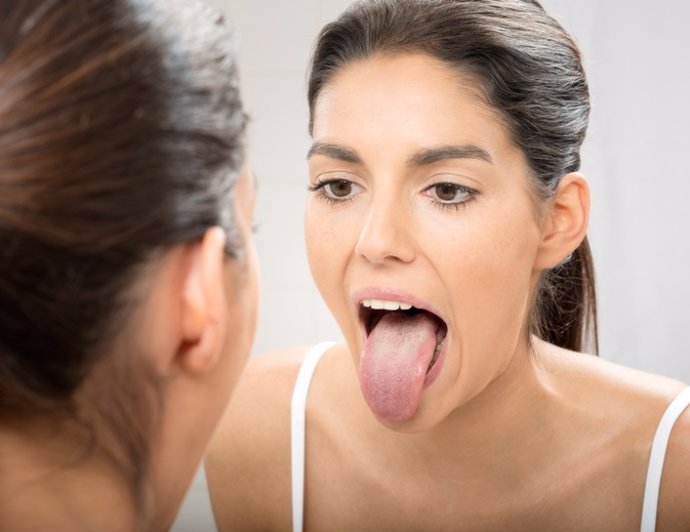 Mujer mirando la lengua en un espejo.